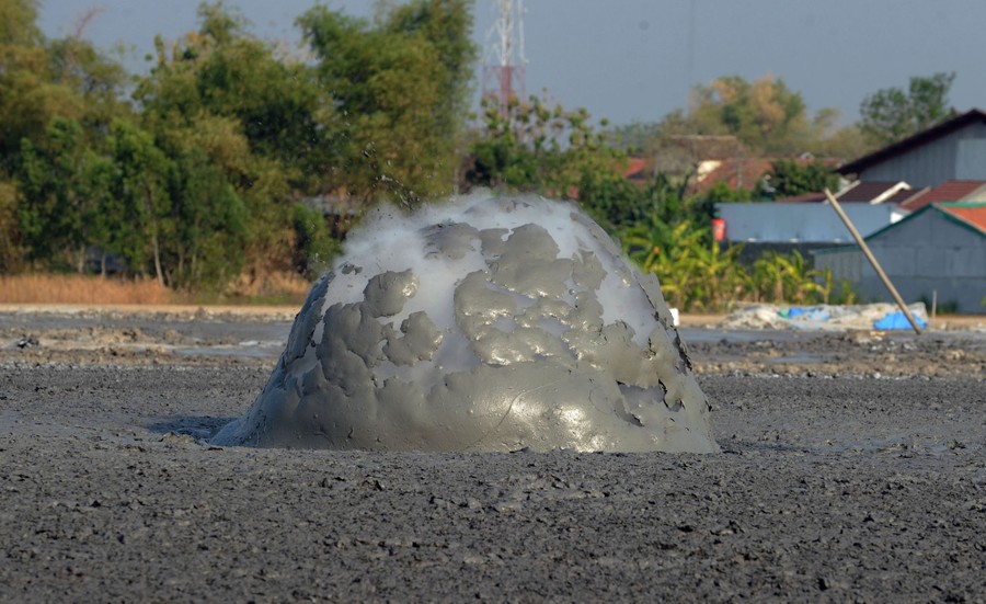 A large bubble of mud filled with steam bursts in a muddy expanse.