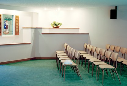 Three rows of chairs sit facing the head of a room in a funeral home. On one chair is a box of tissues.