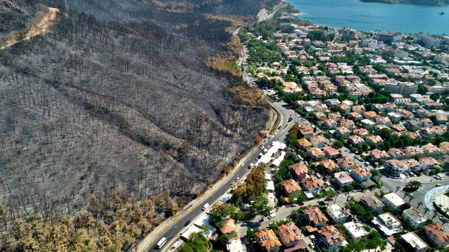 An aerial view shows a scorched hillside on the left, and an apparently untouched neighborhood, on the right.
