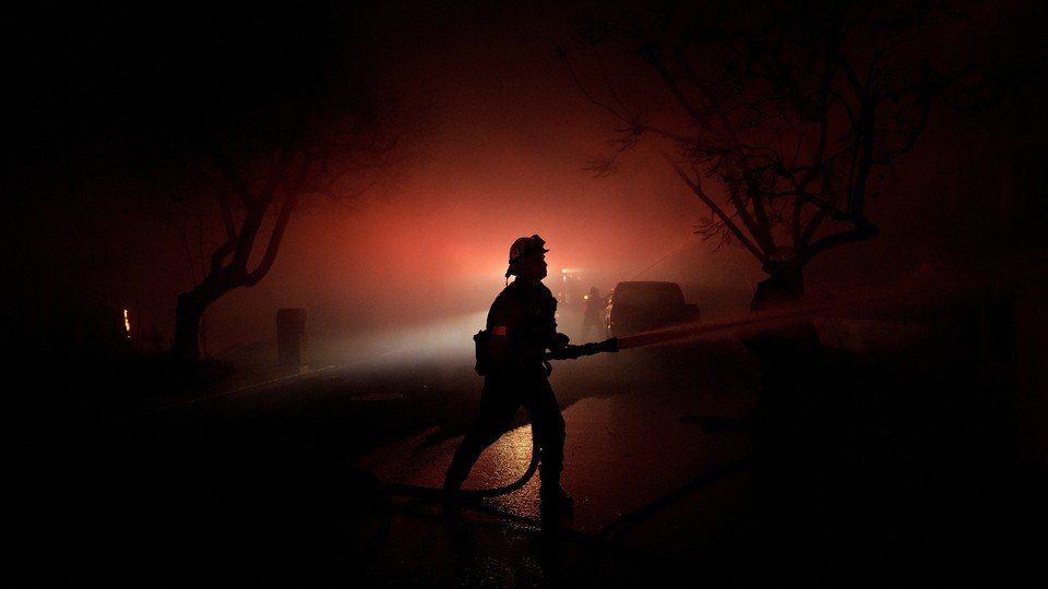 A color photograph of a firefighter at night, backlit by hazy red light.
