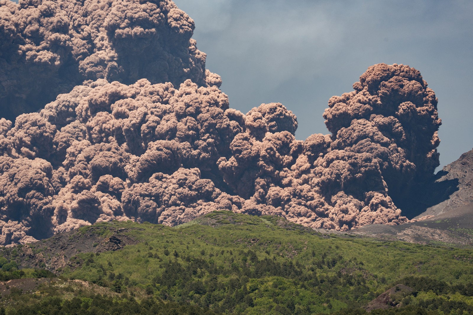 A large plume of brownish-colored ash rises from the top of a volcano.