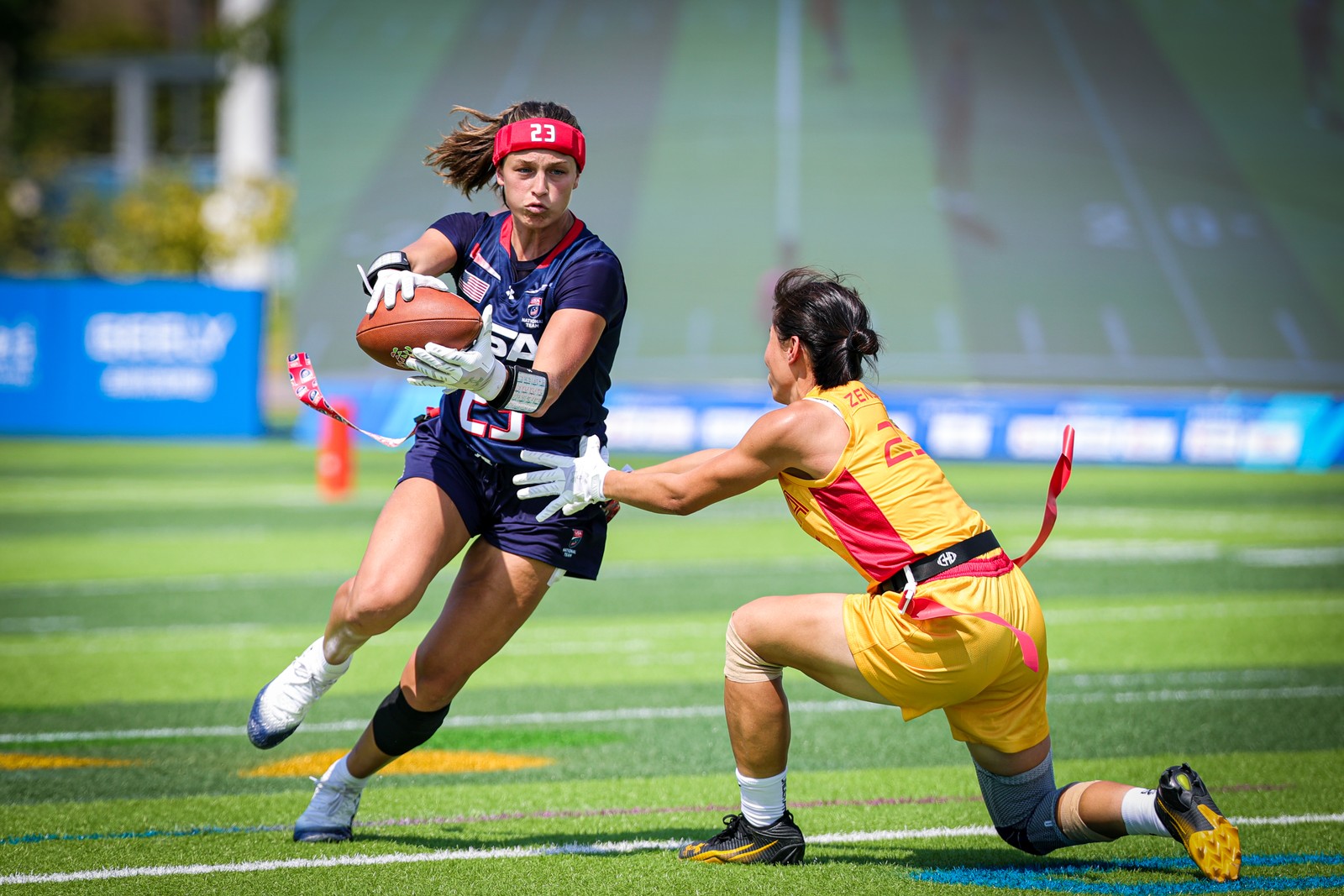 A scene from a flag football match—a competitor reaches out to grab a flag from a member of the opposing team carrying a football.