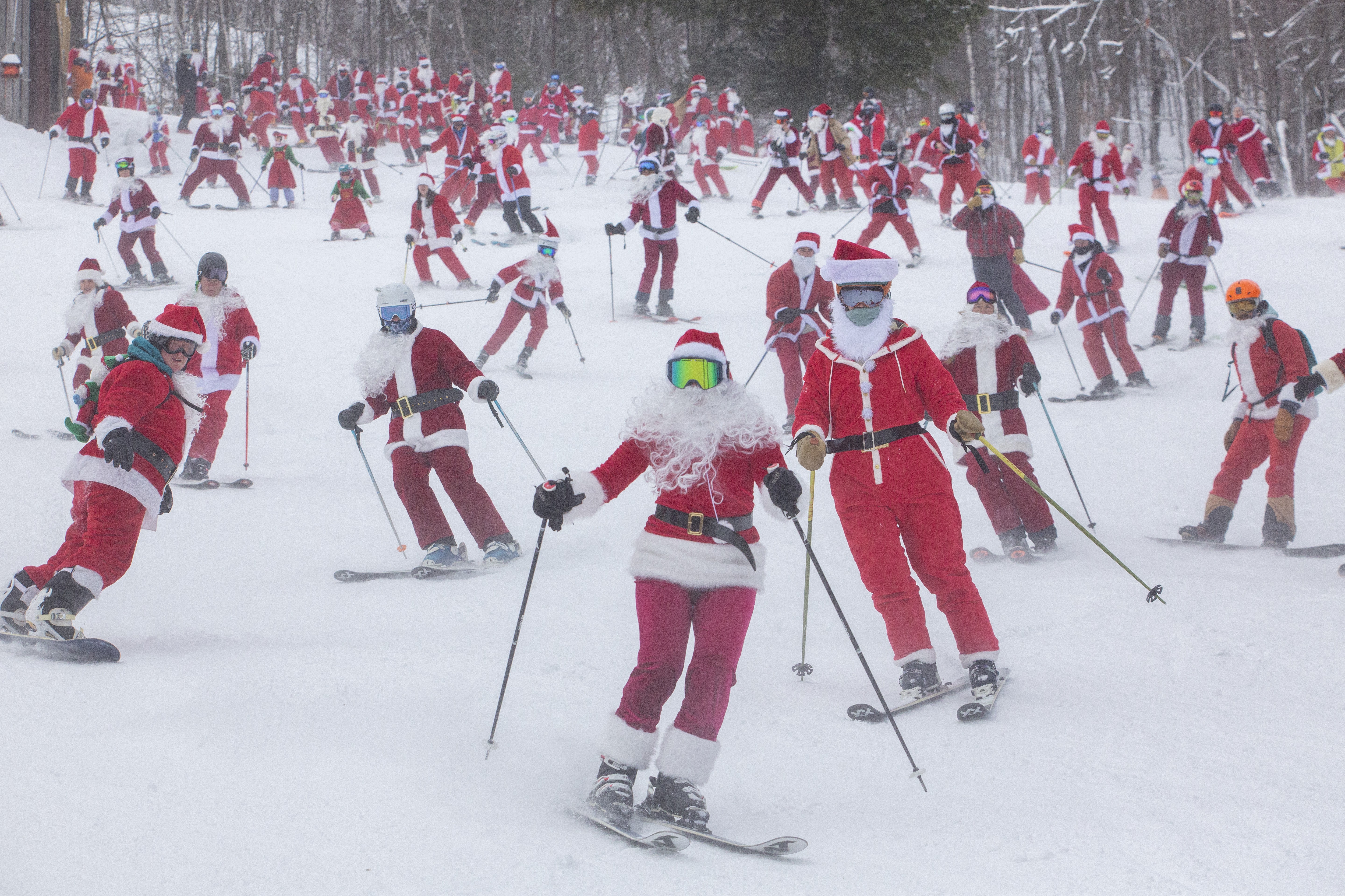 Dozens of people dressed in Santa Claus costumes ski down a slope together.