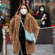 a person wearing a faux fur coat and face mask, with a blue bag over their shoulder