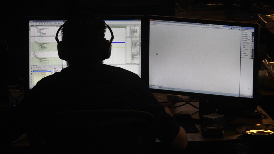 A person wearing headphones in silhouette, backlit by the light of two computer screens with code