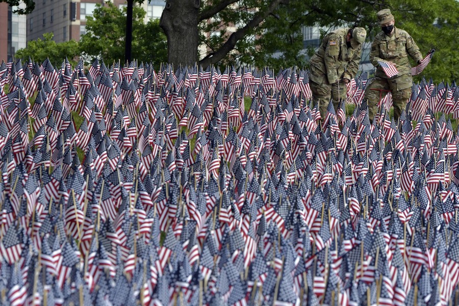 Two soldiers plant small American flags among many hundreds of other flags.