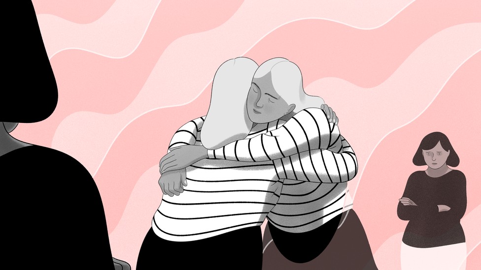 Woman hugging herself in a mirror, with jealous friend in the background.