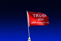 A color photograph of a white pointed tent top with a red "Trump 2024" flag on top