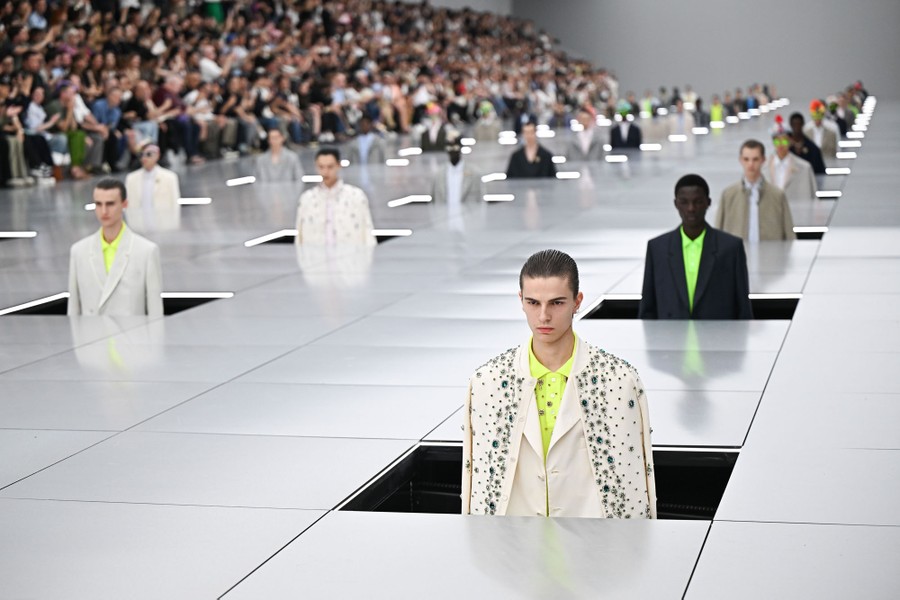 Dozens of models stand in square waist-deep holes in a broad fashion runway.