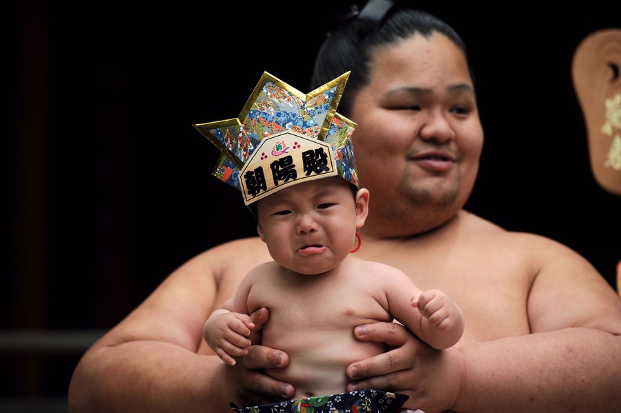 A baby cries as he is carried by a sumo wrestler.