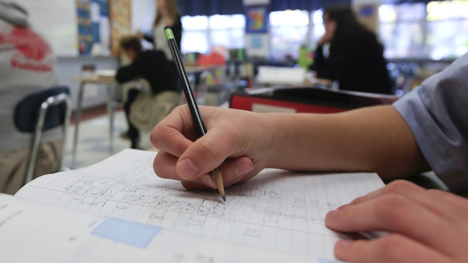 A student writes with pencil on a sheet of notebook paper.