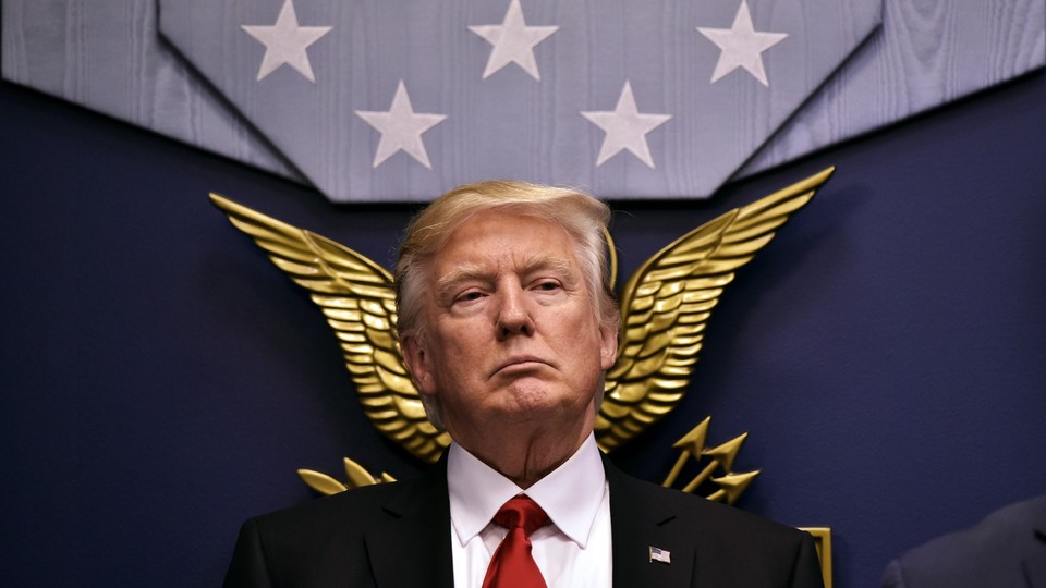 Trump stands in front of a bronze eagle and 5 stars on a flag.