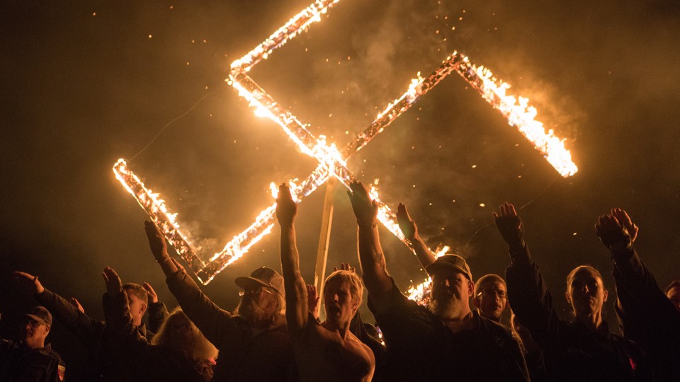 Supporters of the National Socialist Movement give Nazi salutes while taking part in a swastika burning.