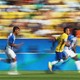 Three soccer players run toward the right side of the frame; the one in the center wears the distinctive yellow jersey of the Brazilian men's national team.