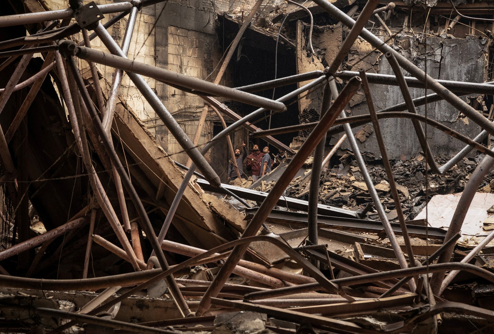 Several people stand inside the ruins of a burned structure, assessing the damage.