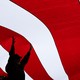 Silhouettes of people hold up a giant flag with red and white stripes