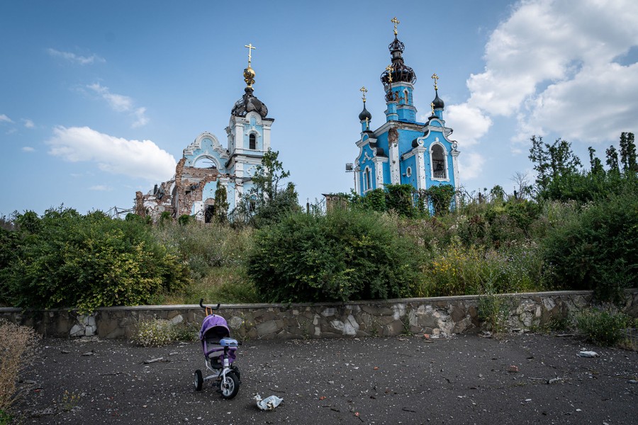 A small stroller sits on pavement in front of two bomb-damaged church structures.