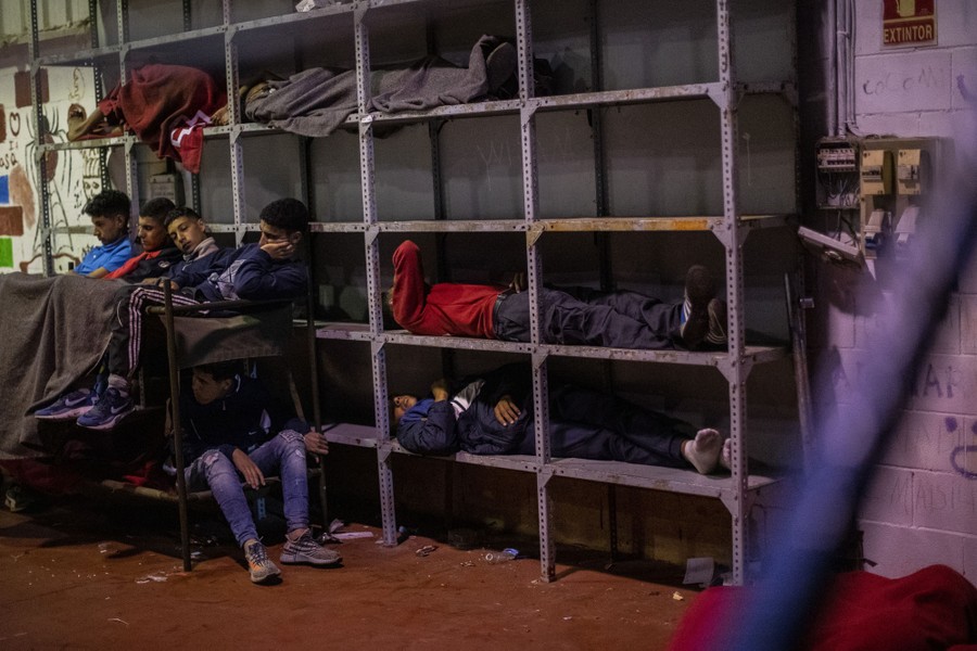 Young men and boys sleep in stacked beds and shelving.