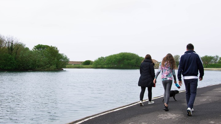 A teenager and her parents walk their dog along a river.