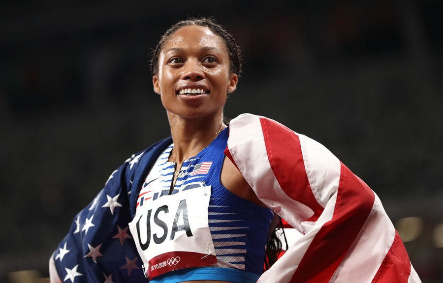 Allyson Felix stands on a track wearing an American flag over her shoulders.