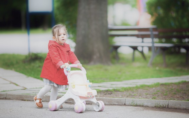 A child pushes a stroller down a street.