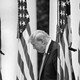 Donald Trump with his head down and American flags in the background
