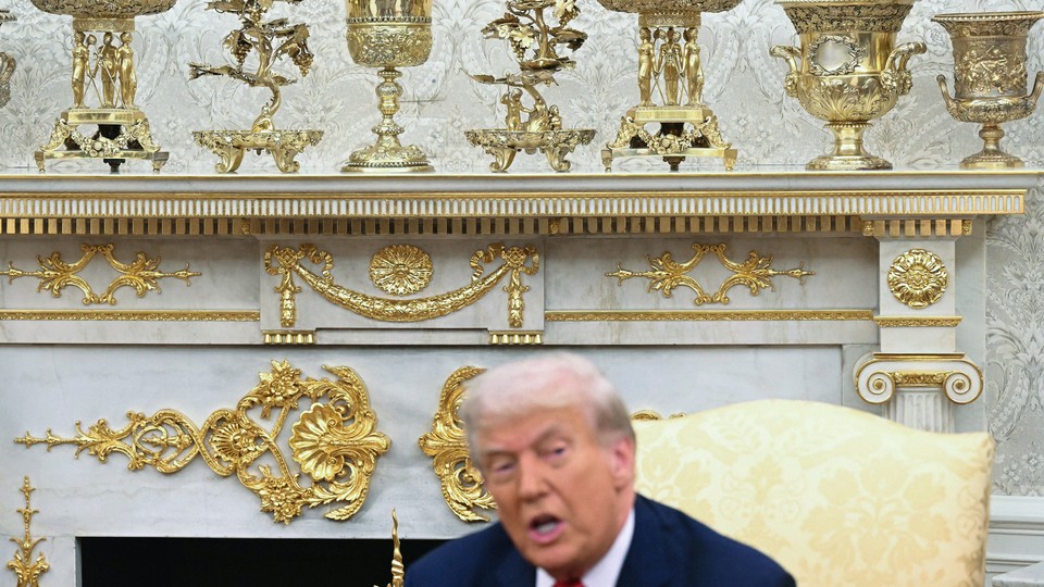A photograph of Donald Trump sitting in front of a gilded, gold mantelpiece.