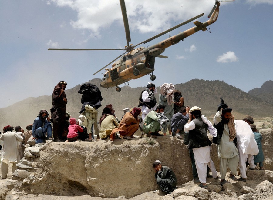 A helicopter lifts off as people below cover their heads.
