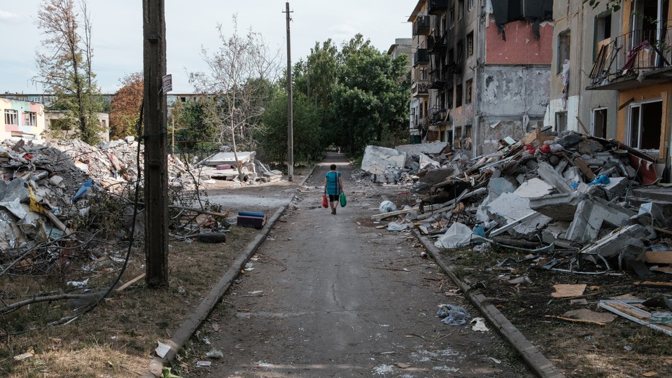 Photo of a woman walking down a road in Ukraine with debris and destroyed buildings around her.