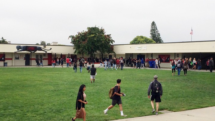 Students walk across a grassy field in front of a school building.