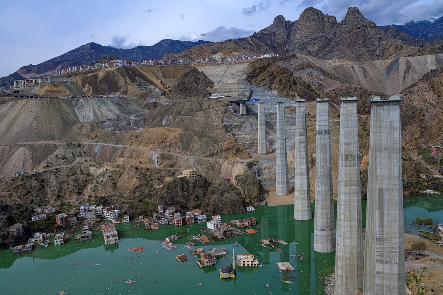 An aerial view of a flooded valley and a tall, under-construction road bridge