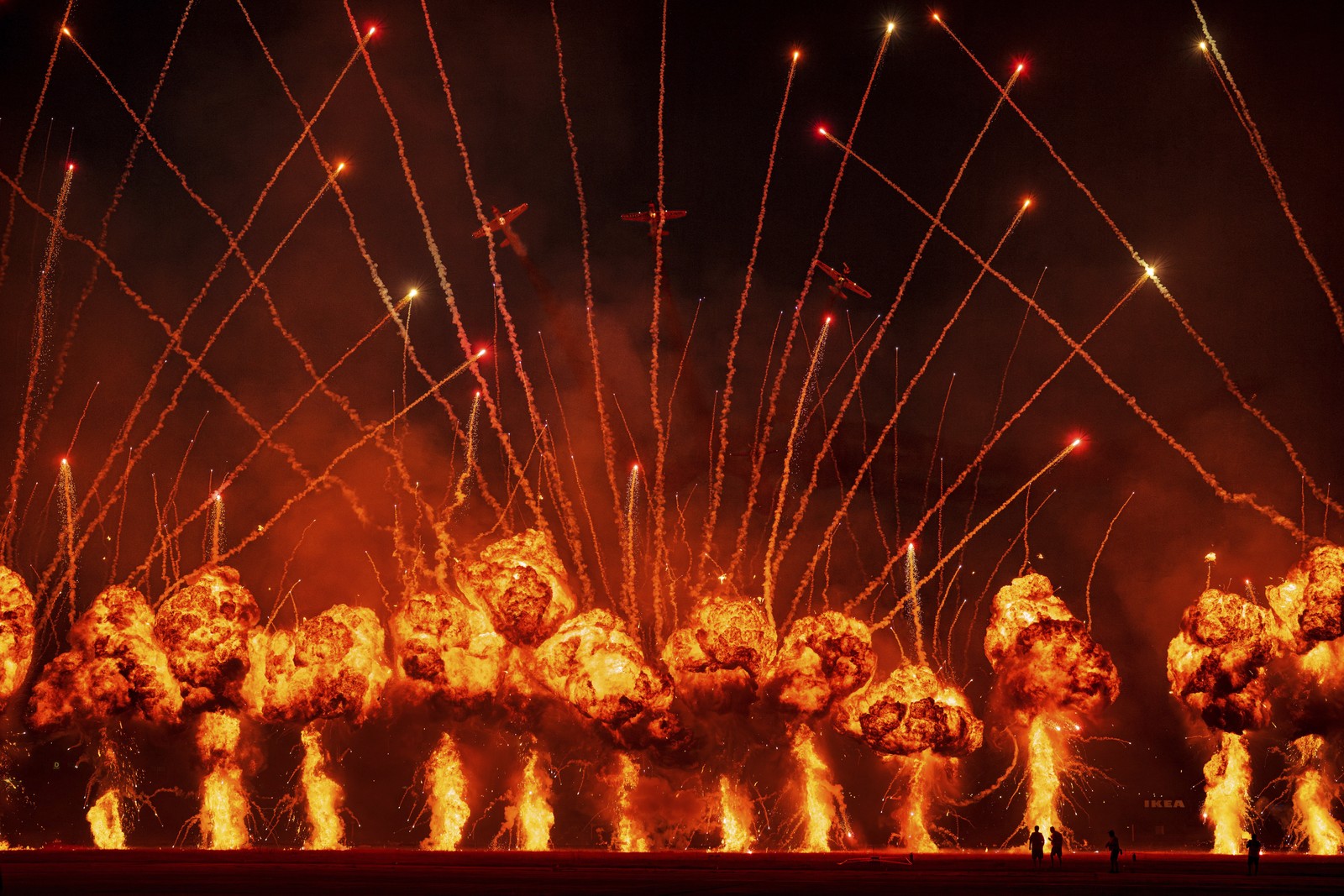 A line of pyrotechnic displays and fireworks erupt as stunt planes fly overhead.
