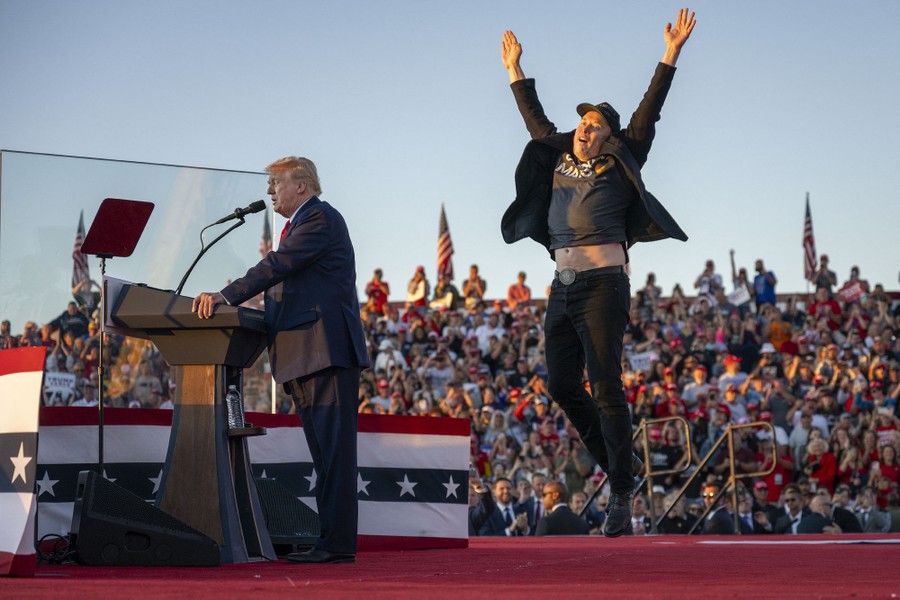 Elon Musk jumps onstage, raising his arms, beside Donald Trump.