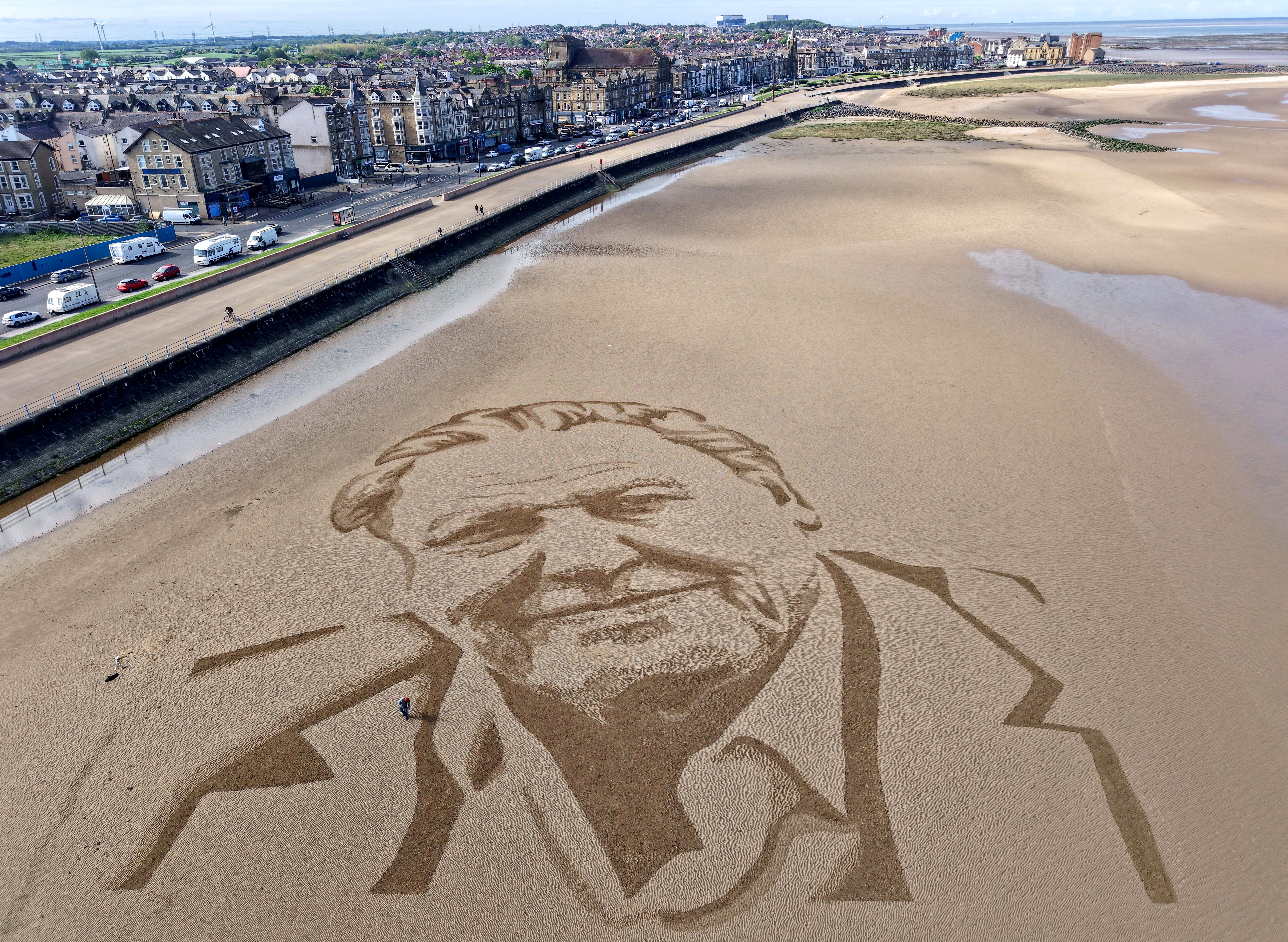 A drone view of a giant sand portrait of David Attenborough on a beach