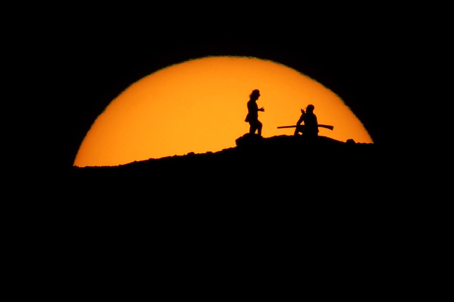 The silhouettes of two people are seen against the distant setting sun.
