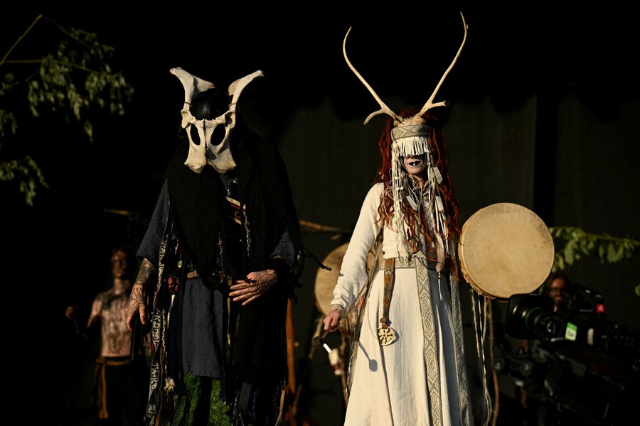 Two performers wearing costumes made partly from bones and antlers stand on a stage.