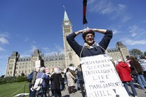 Protester with telescope on head with sign saying, "Desperately seeking intelligent light on Parliament Hill!"