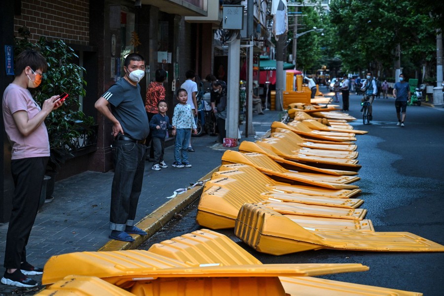 People stand on a sidewalk looking at toppled sections of plastic barriers.
