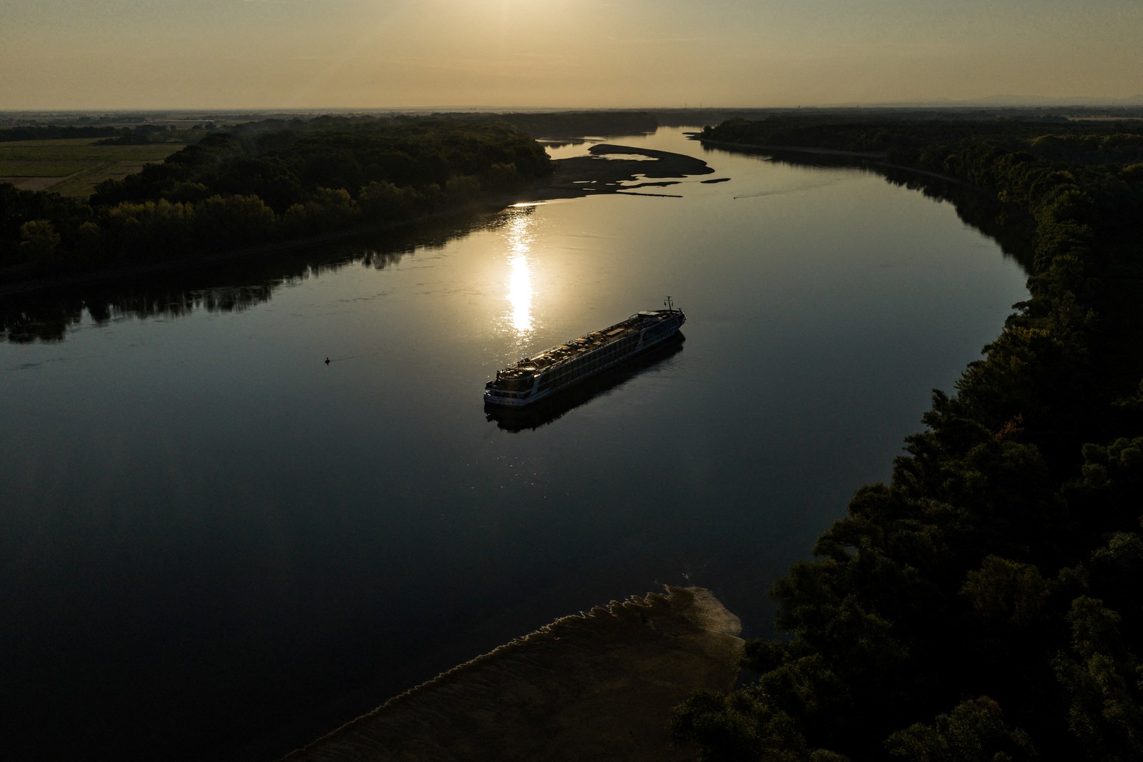 A drone view of a river cruise boat sitting still in the middle of a calm river