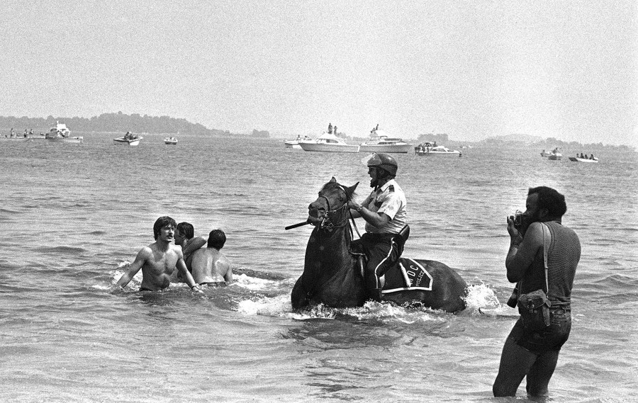 A police officer on horseback rides in shallow water toward several people.