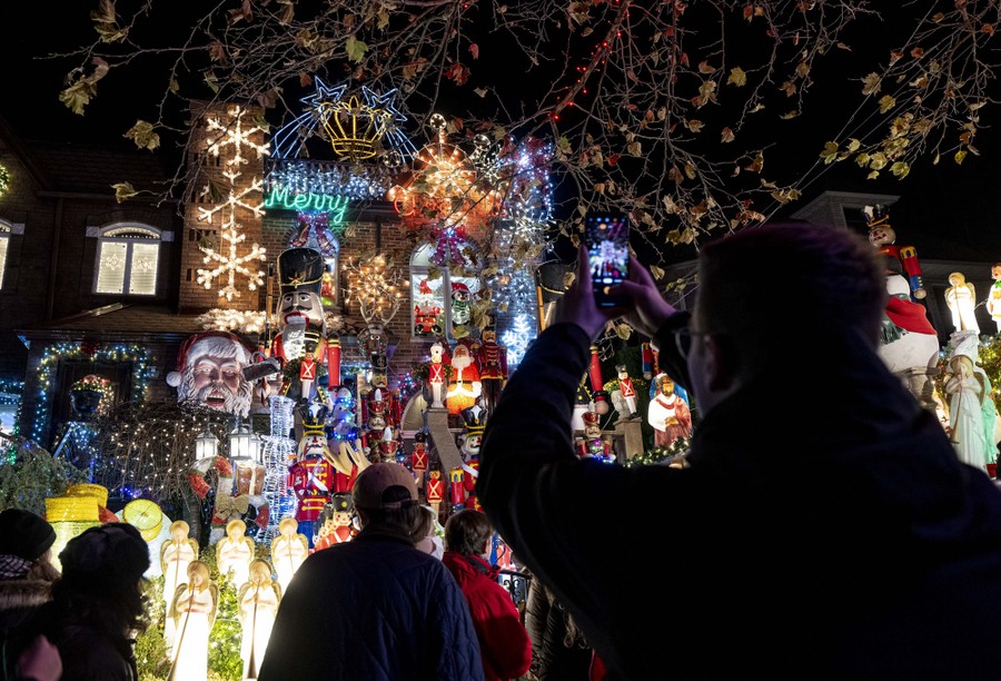People stand outside and take photographs of a home that is densely covered with bright Christmas decorations.