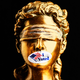 Lady Justice with an "I Voted" sticker covering her mouth