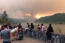 People watch a wildfire burning in a mountain range.