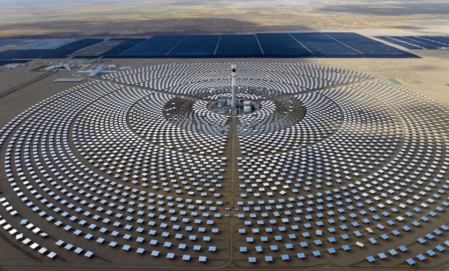 An elevated view of a solar power plant—hundreds of mirrors arrayed in a circle around a central tower in a desert