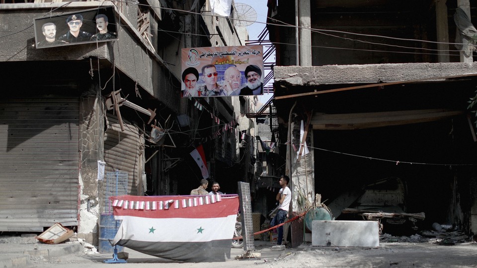Photograph of a ruined street in Damascus with a poster of Khamenei, Assad, and Nasrallah.