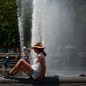A woman sits beside a fountain on a hot day.