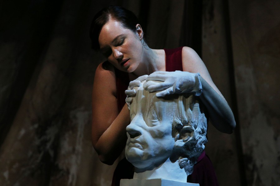 A performer pulls at a flexible stage prop made to look like a marble bust.