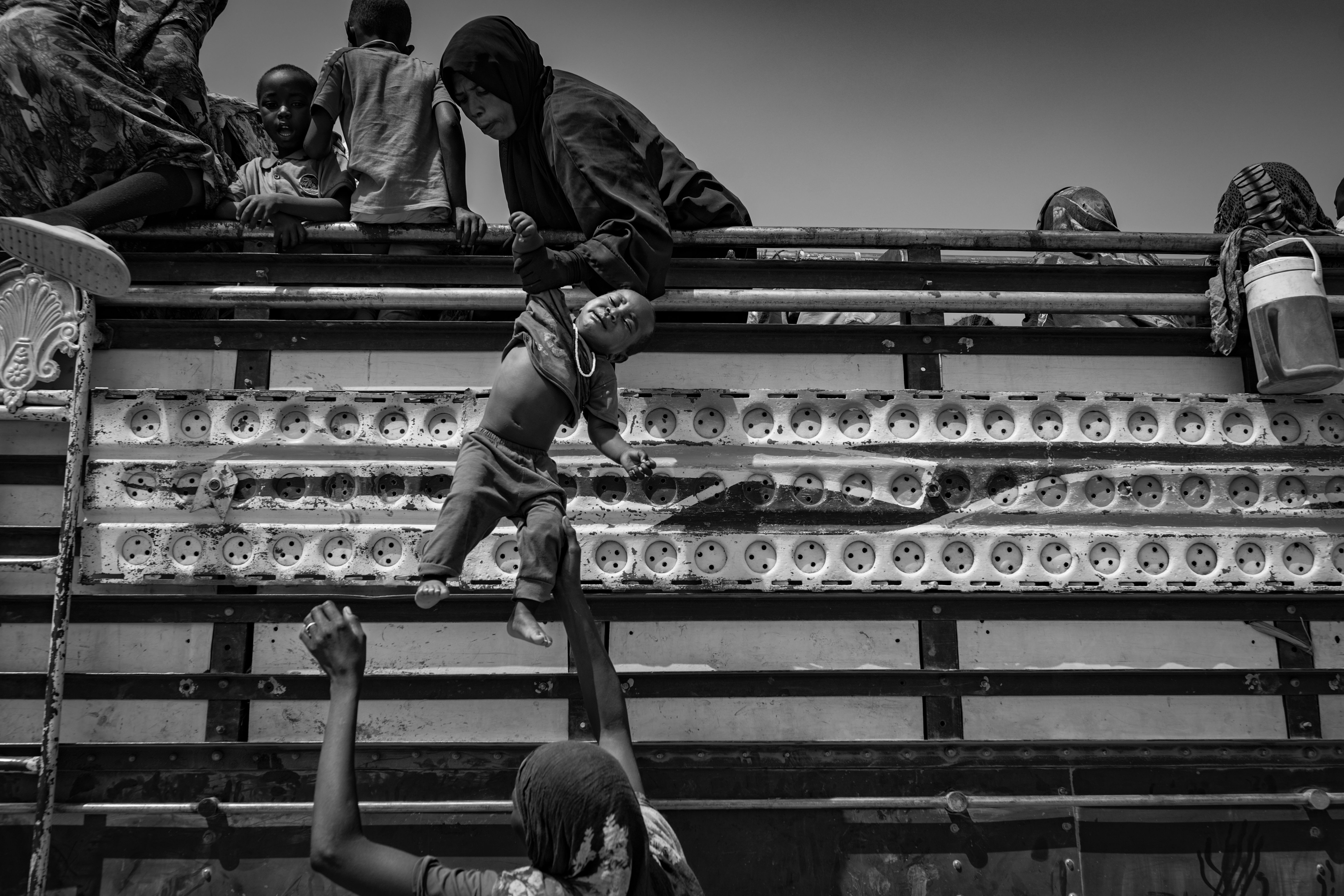 Picture of a Sudanese refugee in Tiné passing a child up to another woman as dozens of new arrivals pile into an open truck.