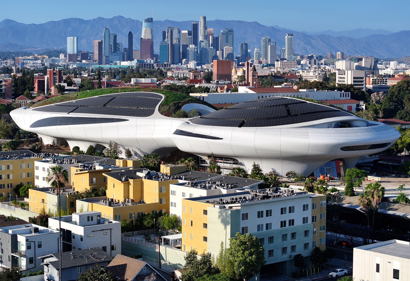 An aerial view of a large spaceship-shaped building, seen in front of the Los Angeles skyline