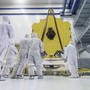 NASA employees, dressed in white uniforms, look up at the gold-plated mirrors of the James Webb Space Telescope.